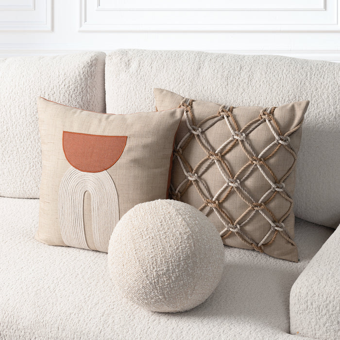 Three decorative throw pillows arranged on a textured cream sofa: a square pillow with a terracotta and cream abstract design, a square pillow with a beige rope lattice pattern, and a round textured cream pillow in front.
