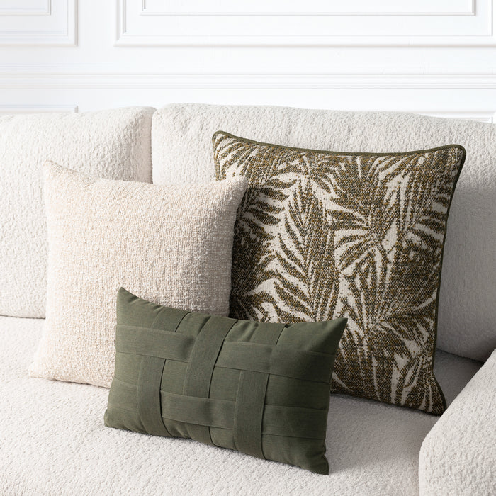 Three decorative throw pillows arranged on a textured cream boucle sofa: a large square pillow with an olive and cream palm leaf pattern, a smaller square cream pillow, and a small rectangular olive green woven lumbar pillow.
