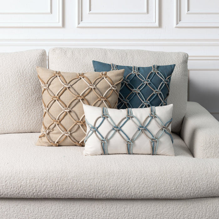 Three decorative throw pillows with geometric rope-knit patterns arranged on a textured light beige sofa against a white paneled wall.