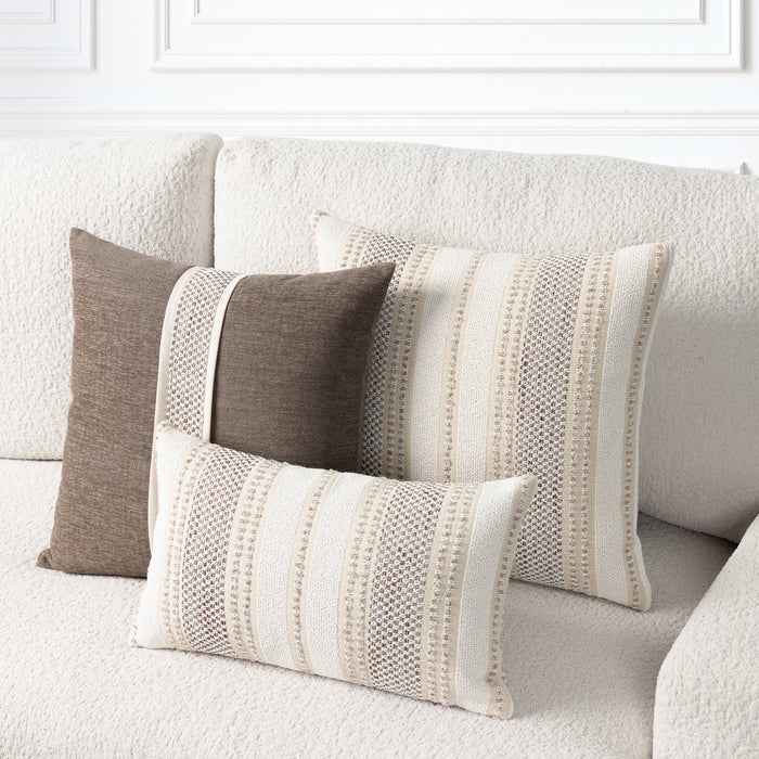 Three decorative throw pillows in neutral tones arranged on a textured cream sofa. Two larger pillows and one smaller lumbar pillow feature vertical stripe patterns in cream, beige, and taupe, with one solid taupe pillow on the left.