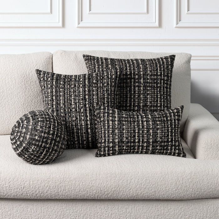 Three textured throw pillows in a black and off-white woven pattern arranged on a light beige boucle sofa against a white paneled wall.