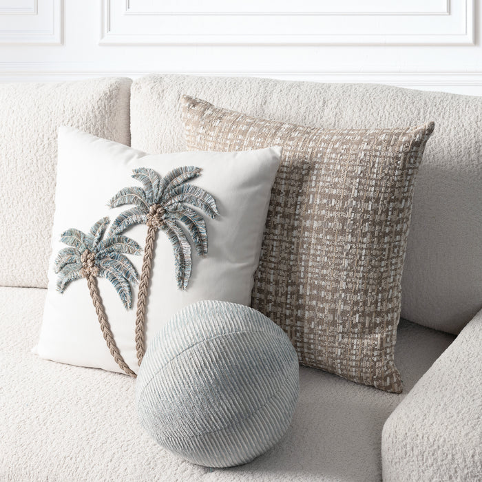 A styled home decor scene showing two decorative throw pillows and a round lumbar pillow on a textured beige sofa. The front pillow is off-white with a raised palm tree motif in blue-gray and tan.