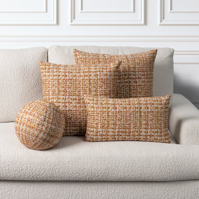 Three textured throw pillows in a warm orange and cream bouclé pattern arranged on a light beige sofa against a white paneled wall.