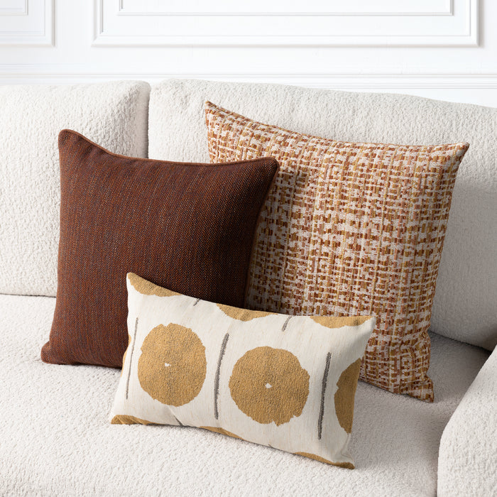 Three decorative throw pillows arranged on a textured cream sofa: a square dark brown pillow, a square tan and brown woven pattern pillow, and a smaller rectangular cream pillow with large tan circular motifs and thin gray vertical lines.
