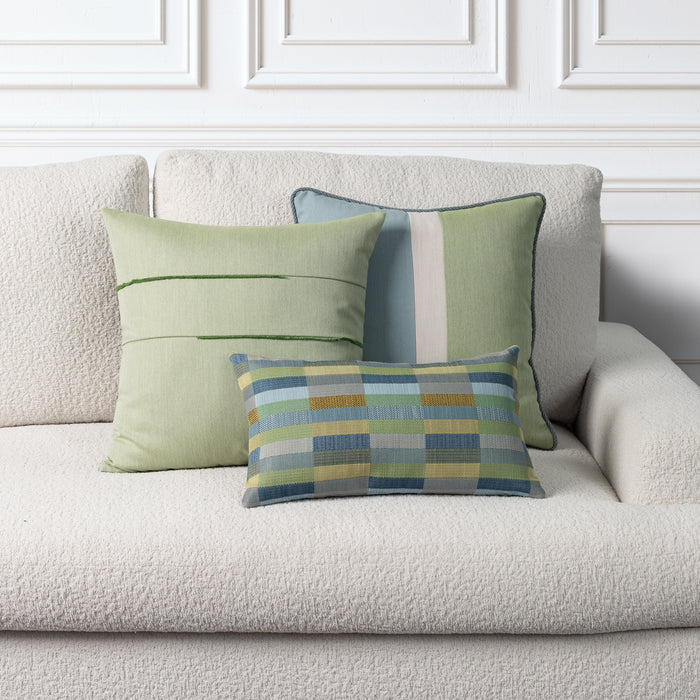 Three decorative throw pillows in shades of sage green, blue, and yellow are arranged on a textured cream boucle sofa against a white paneled wall.