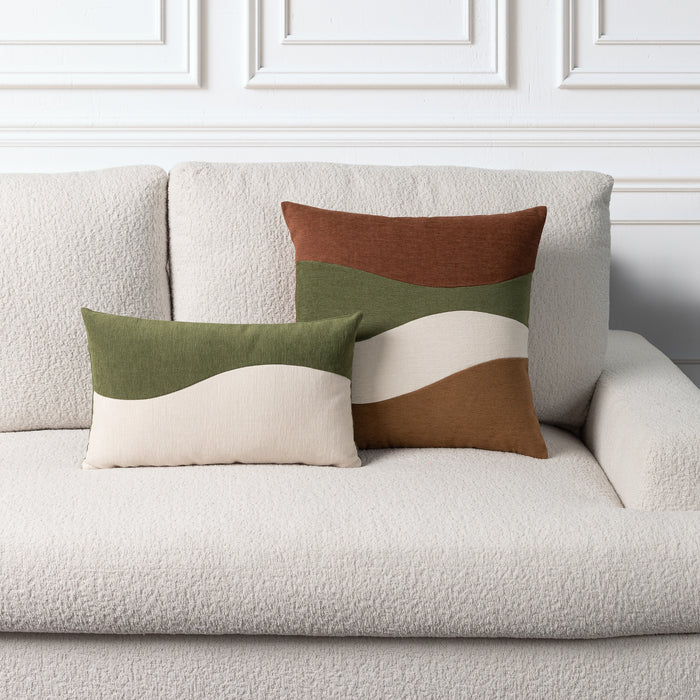 Two decorative throw pillows with wavy color-blocked stripes in olive green, cream, and brown, styled on a textured off-white boucle sofa against a white paneled wall.