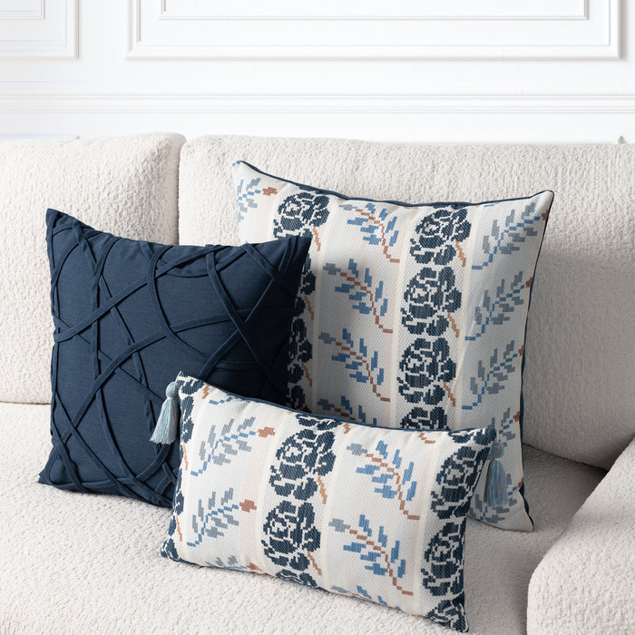 Three decorative throw pillows arranged on a cream boucle sofa. One pillow is dark navy blue with a crisscross textured pattern, and two other pillows feature a cream background with navy floral motifs and blue leaf accents.