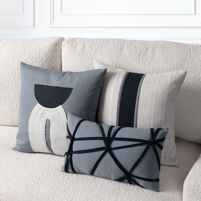 Three decorative throw pillows in gray, beige, and indigo tones arranged on a textured cream sofa. The pillows feature abstract geometric and striped patterns.