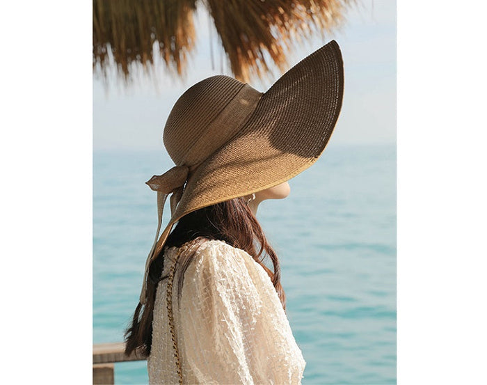Woman wearing a wide-brim straw sun hat with a large floppy brim, perfect for summer beach or outdoor sun protection.