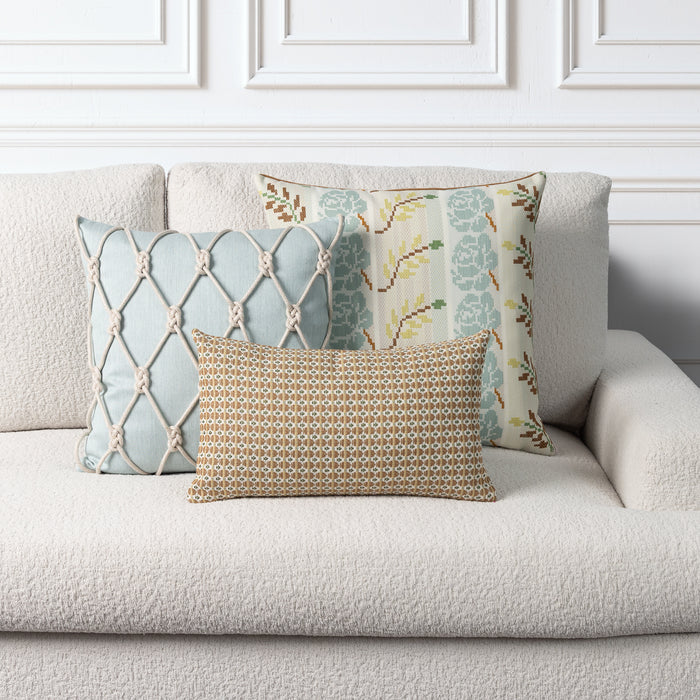 Three decorative throw pillows arranged on a light beige textured sofa against a white paneled wall. The front pillow is rectangular with a gold, brown, and beige geometric pattern.