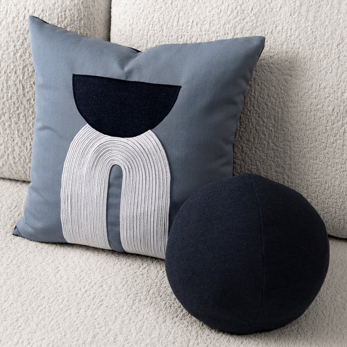 Decorative pillow with abstract design on a couch next to a round black pillow.