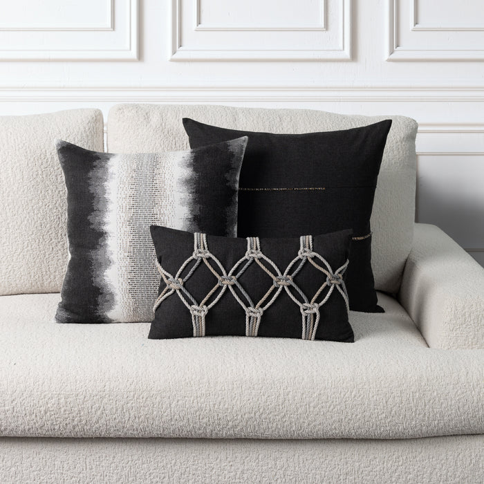 Three decorative throw pillows in black and white displayed on a textured cream boucle sofa against a white paneled wall.