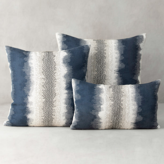 Three blue and gray striped pillows on a neutral background