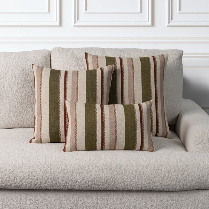 Three striped throw pillows in beige, brown, and olive green tones arranged on a light beige textured sofa against a white paneled wall.