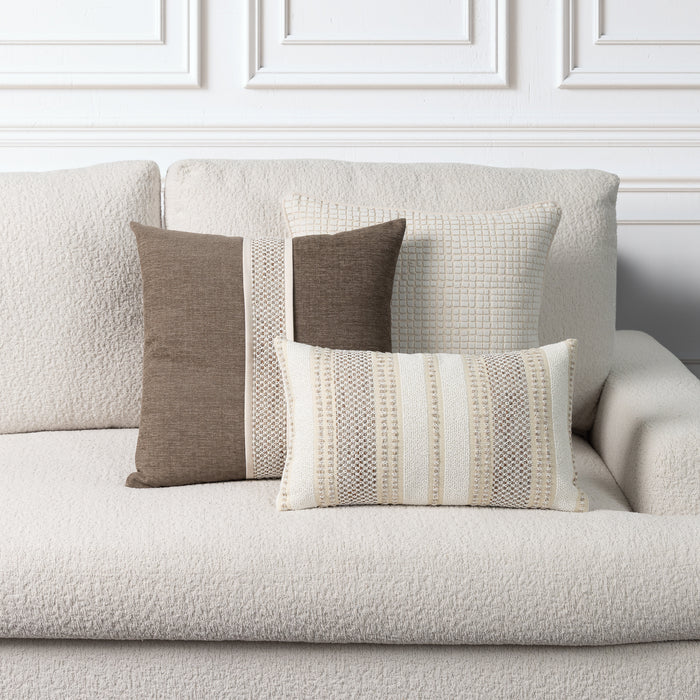 A set of textured throw pillows in neutral tones of beige, cream, and taupe arranged on a light beige boucle sofa against a white paneled wall.