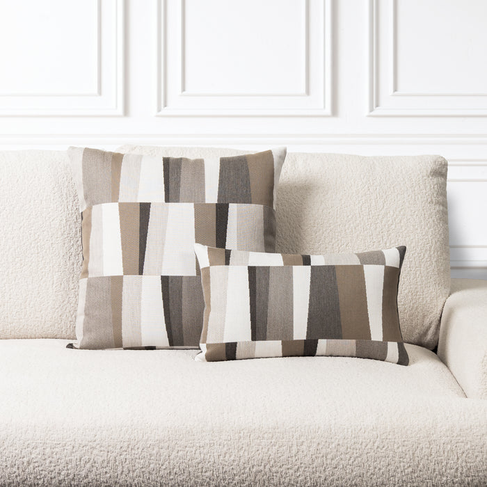 Two rectangular throw pillows with a geometric stripe pattern in beige, brown, gray, and white, styled on a textured cream sofa against a white paneled wall.