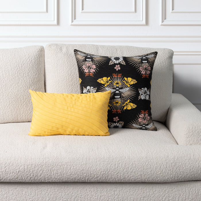 Two decorative throw pillows on a textured light beige sofa: a bright yellow rectangular pillow in front and a black square pillow behind with a floral and bird pattern in yellow, white, and pink.