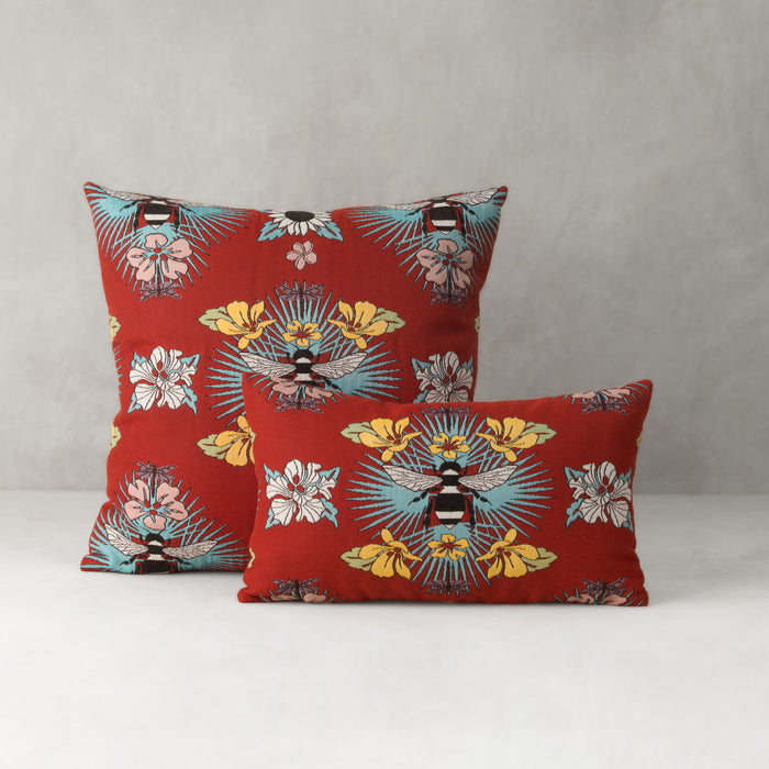 Two red pillows with floral and bee pattern on a gray background