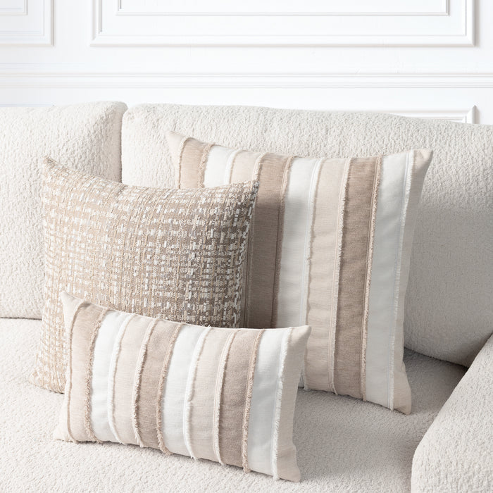 Three decorative throw pillows in neutral beige, cream, and taupe tones arranged on a textured cream sofa against a white paneled wall.