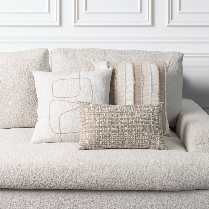 Three decorative throw pillows in neutral beige and cream tones arranged on a textured boucle sofa against a white paneled wall.